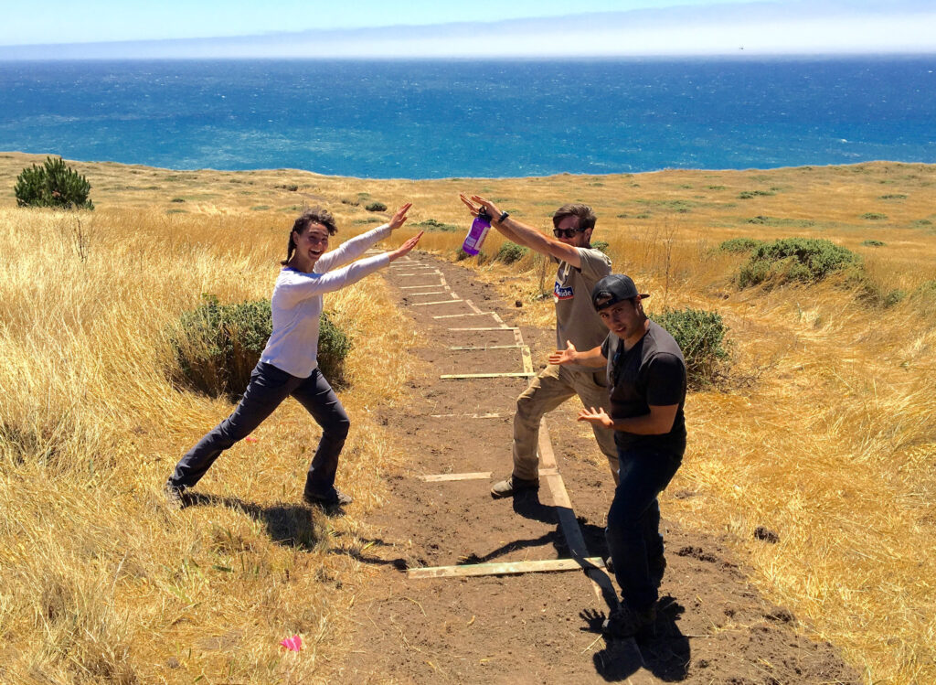 Three teens smiling and holding arms over a newly constructed trail