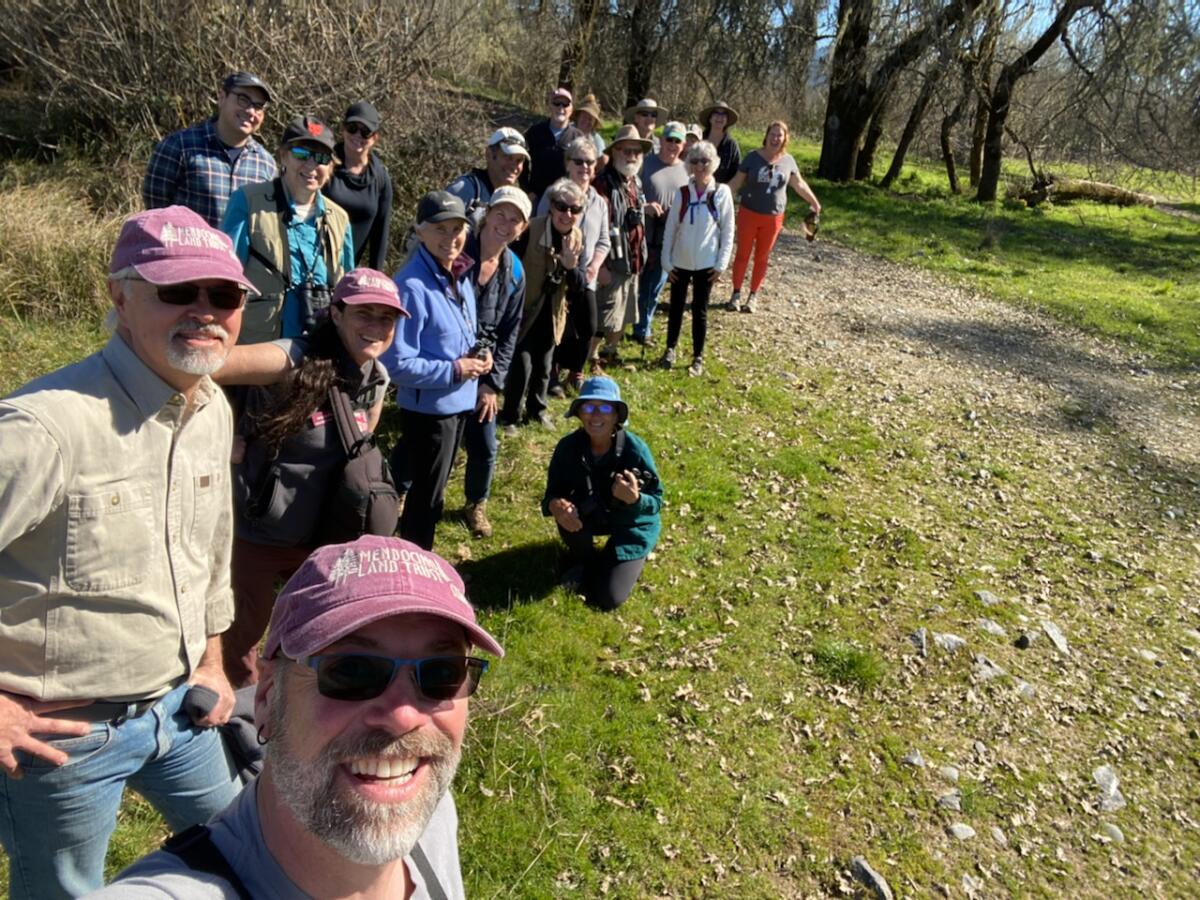 A photo of a group outdoors taken as a selfie by a man with a long arm