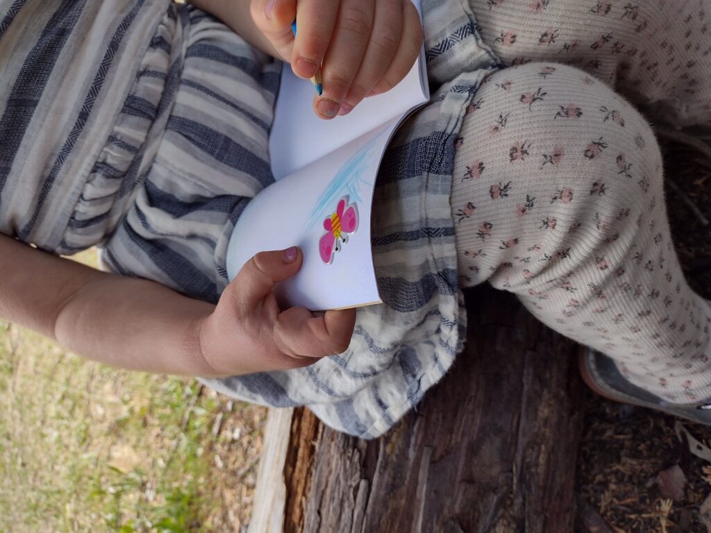 5 year old girl drawing in a notebook around a butterfly sticker