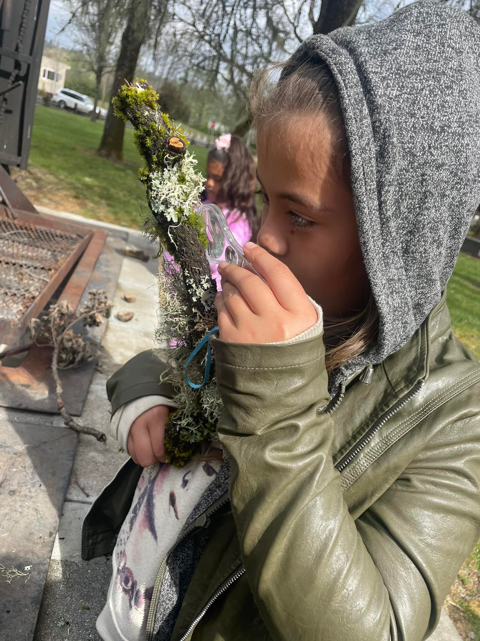 Young girl with a magnifier looking at moss on a stick