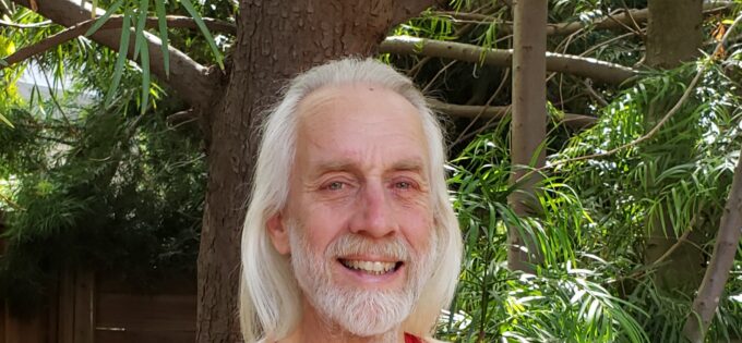 Smiling man with long white hair wearing a red tshirt