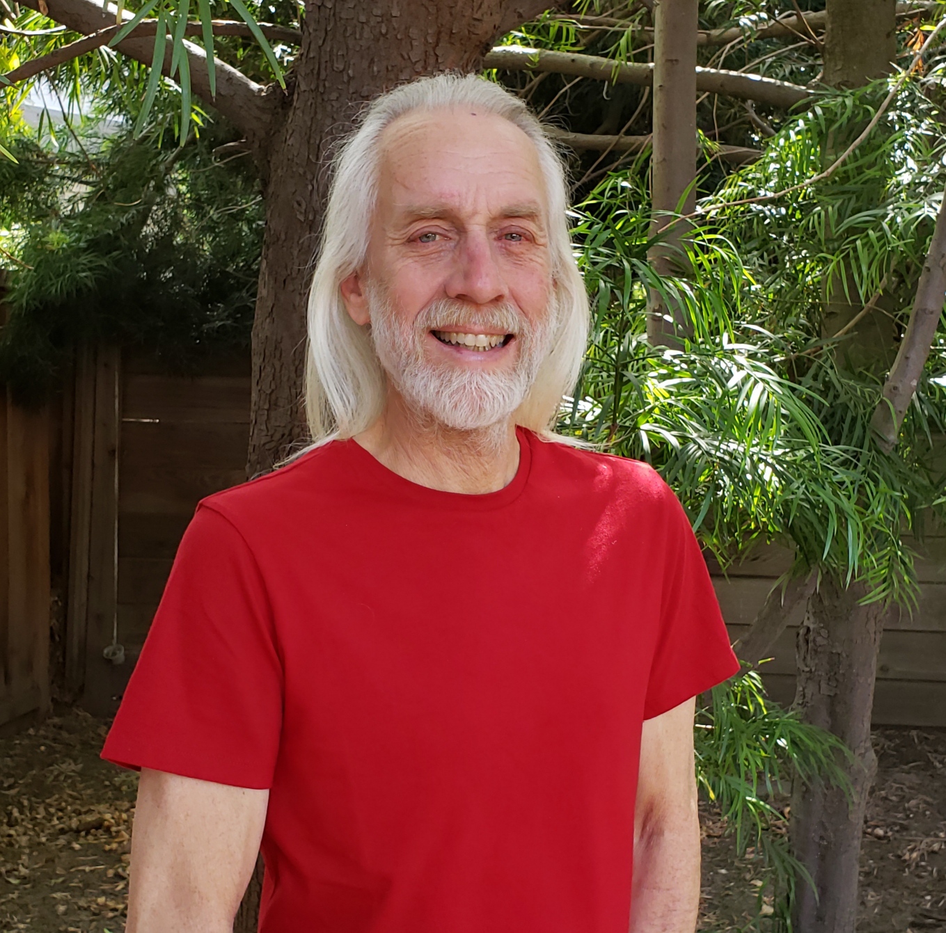 Smiling man with long white hair wearing a red tshirt